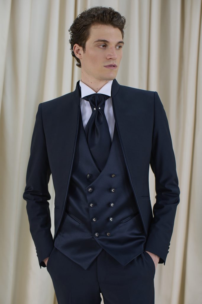 In questa foto, un uomo posa con un abito blu lucido e gilet doppiopetto, completato da una cravatta larga e strutturata. L’immagine rappresenta una proposta elegante e audace su come scegliere abito da sposo dallo stile regale.