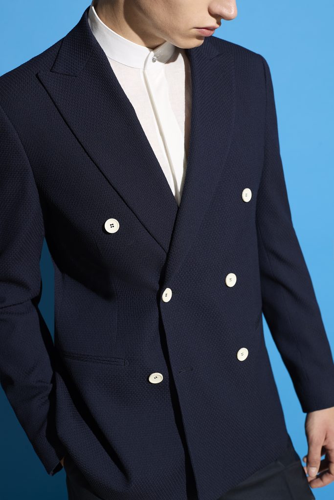 In questa foto, si vede un primo piano della giacca blu doppiopetto con bottoni bianchi, evidenziando i dettagli sartoriali. Un ottimo riferimento visivo per chi si chiede come scegliere abito da sposo dal taglio sartoriale e originale.