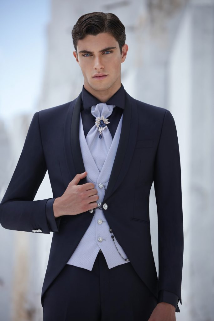 In questa foto lo sposo indossa un abito blu notte con panciotto chiaro, camicia scura e cravatta gioiello, mettendo in evidenza il contrasto cromatico, utile per orientarsi su come scegliere abito da sposo elegante e distintivo.