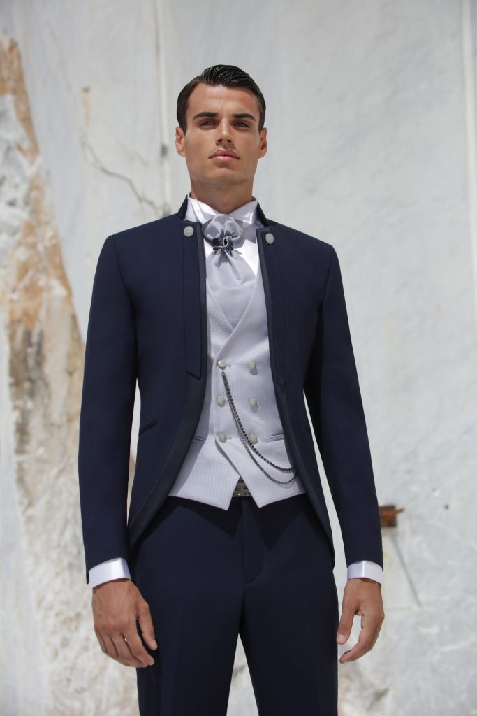 In questa foto un completo blu scuro con collo alla coreana, panciotto chiaro e spilla gioiello al collo valorizza una linea moderna e pulita, ideale per chi vuole capire come scegliere abito da sposo contemporaneo.