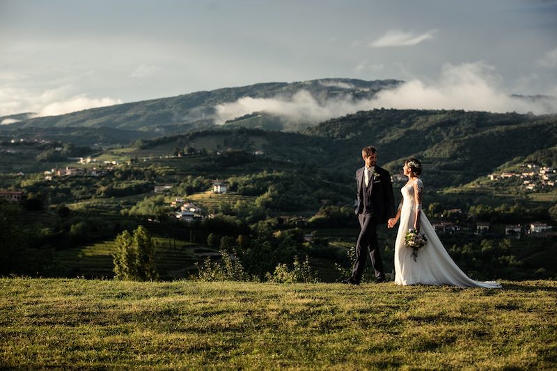 In questa foto, due sposi si guardano negli occhi e camminano su un prato. Sullo sfondo si intravede il paesaggio del Castello Formentini a San Floriano del Collio in Friuli Venezia Giulia