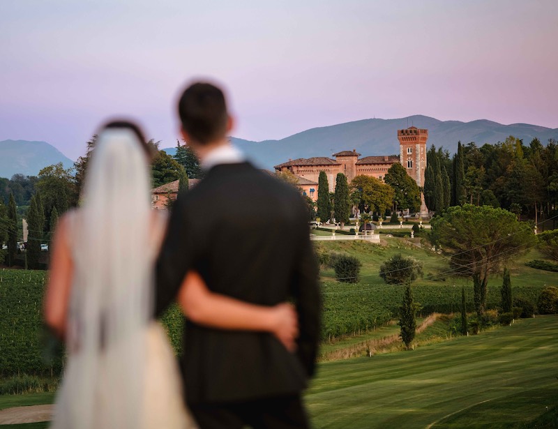 In questa foto, due sposi di spalle e fuori fuoco mentre osservano il Castello di Spessa in Friuli Venezia Giulia