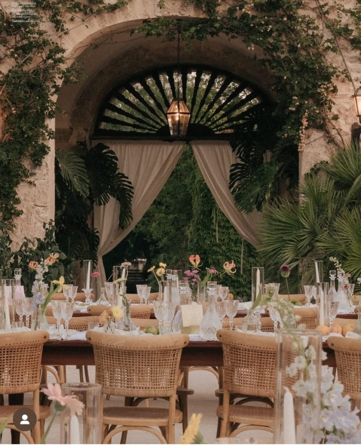 In questa foto, un elegante cortile con archi in pietra e vegetazione rampicante ospita tavoli apparecchiati con cristalli, fiori freschi dai colori pastello e sedute in legno intrecciato. L’atmosfera è mediterranea e sofisticata, in linea con le tendenze allestimenti matrimonio 2026 che valorizzano il fascino delle location storiche.