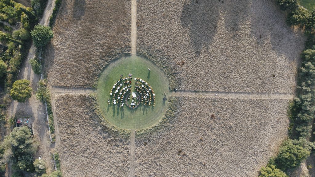 In questa foto, un’inquadratura aerea mostra una cerimonia nuziale immersa nella natura, con gli invitati disposti in cerchio su un prato al centro di una radura. Un esempio perfetto delle tendenze allestimenti matrimonio 2026 che valorizzano la disposizione immersiva e simbolica dello spazio.