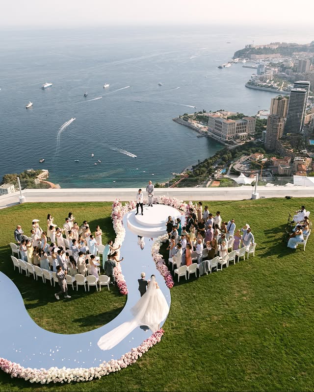 In questa foto, una cerimonia su prato vista mare si distingue per una passerella lucida e specchiata a forma di “S”, contornata da fiori rosa e bianchi. Il colpo d’occhio scenografico incarna al meglio le tendenze allestimenti matrimonio 2026, che celebrano il design teatrale e l’effetto wow.