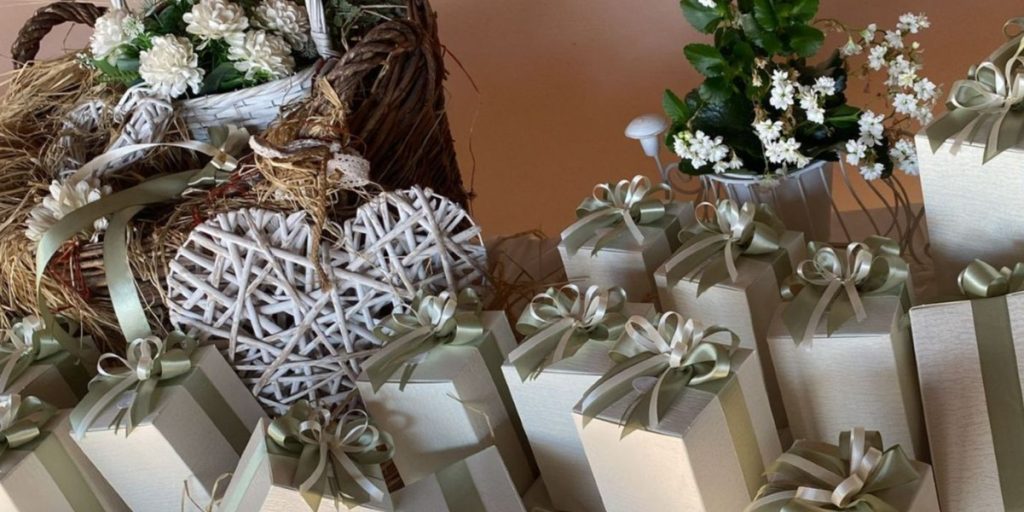 In questa foto si vede una delle Bomboniere di Sabrina presentata come un allestimento completo: scatole rettangolari color avorio con nastri verde salvia, disposte su basi in legno e accompagnate da elementi naturali e floreali.