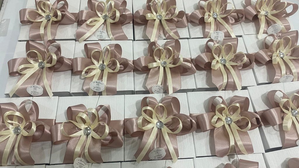 In questa foto si vede una delle Bomboniere di Sabrina formata da scatoline bianche disposte in modo ordinato, decorate con grandi fiocchi in nastro cipria e avorio, arricchiti da un elemento brillante centrale.