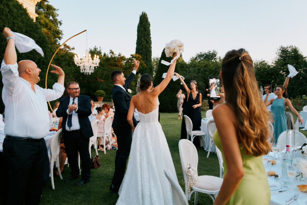 In questa foto si vede una delle caratteristiche dei matrimoni delle nuove coppie, con gli sposi che festeggiano tra gli invitati in un giardino mentre vengono fotografati da un'invitata con lo smartphone