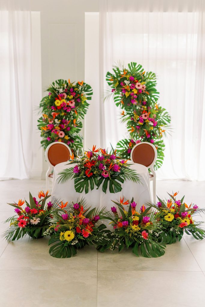 In questa foto si vede una delle tendenze Allestimenti floreali 2026: l’ispirazione tropicale prende il centro della scena con composizioni rigogliose di foglie di monstera e fiori esotici in rosa, arancio e giallo, perfette per cerimonie dallo spirito vivace e moderno.