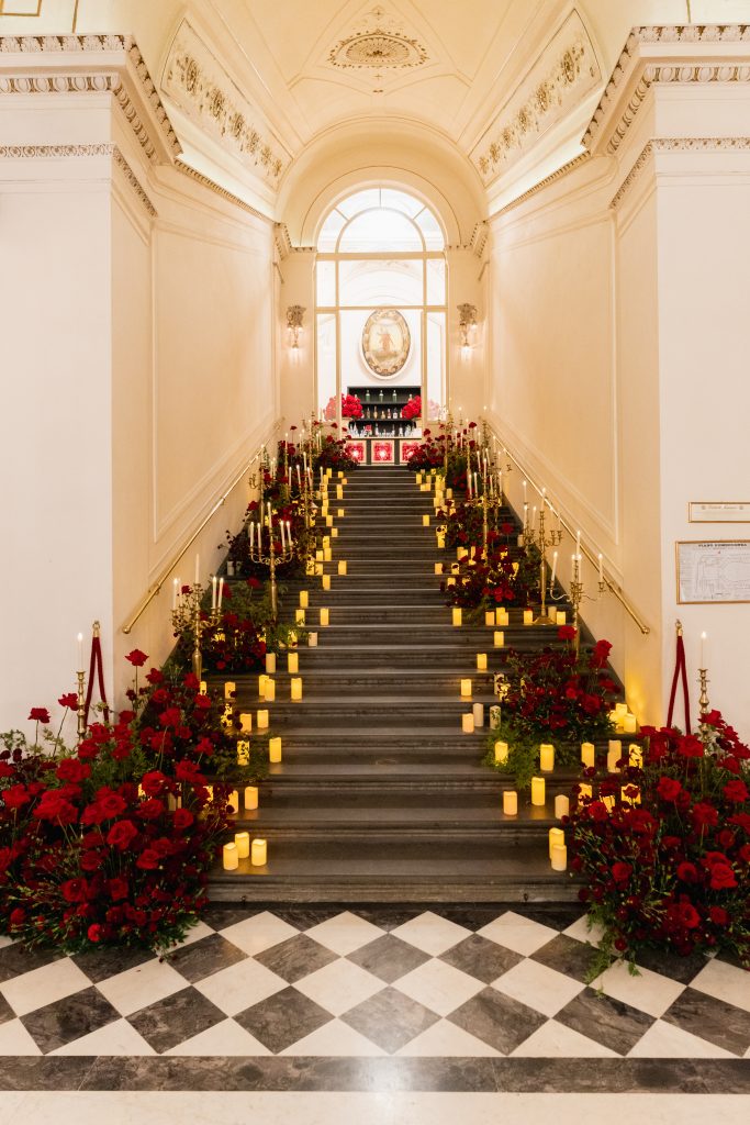 In questa foto si vede una delle tendenze allestimenti location matrimonio 2026: una scalinata monumentale allestita con decine di candele accese e abbondanti composizioni di rose rosse. L’effetto è teatrale e avvolgente, perfetto per ingressi o momenti fotografici.