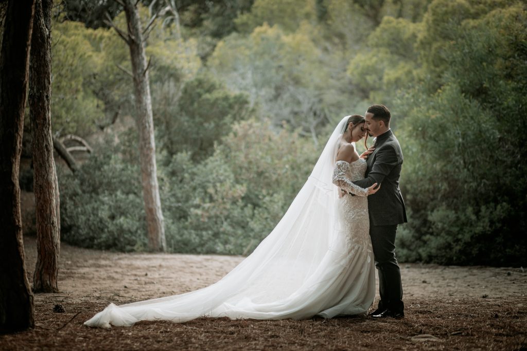 In questa foto si vede una delle fotografie di matrimonio di Davide Meli, una coppia di sposi abbracciata in un bosco, con il lungo velo della sposa disteso a terra e alberi verdi tutt’intorno.