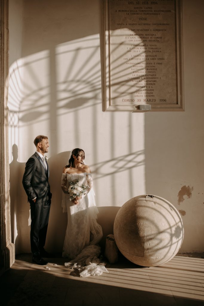 In questa foto si vede una delle fotografie di matrimonio di Davide Meli, una coppia di sposi in un interno storico, accanto a una grande sfera in pietra, attraversati da ombre geometriche proiettate dalla luce naturale.