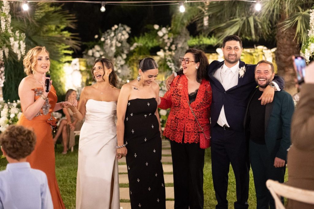 In questa foto si vede uno degli allestimenti de Le Farfalle in Fiore - Angela Crupi: un momento di festa serale all’aperto con il team e gli sposi. L’illuminazione calda e la vegetazione esotica fanno da cornice a un’atmosfera rilassata e gioiosa.