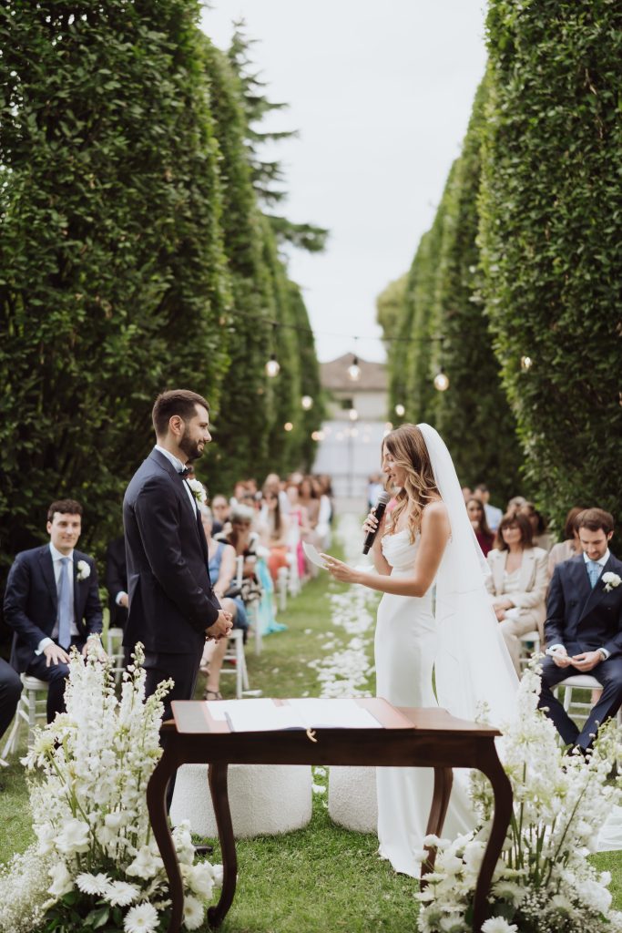 In questa foto si vede una delle caratteristiche dei matrimoni Gen Z, con una coppia che si scambia le promesse durante una cerimonia all’aperto tra alte siepi verdi, in un contesto essenziale, intimo e immerso nella natura.