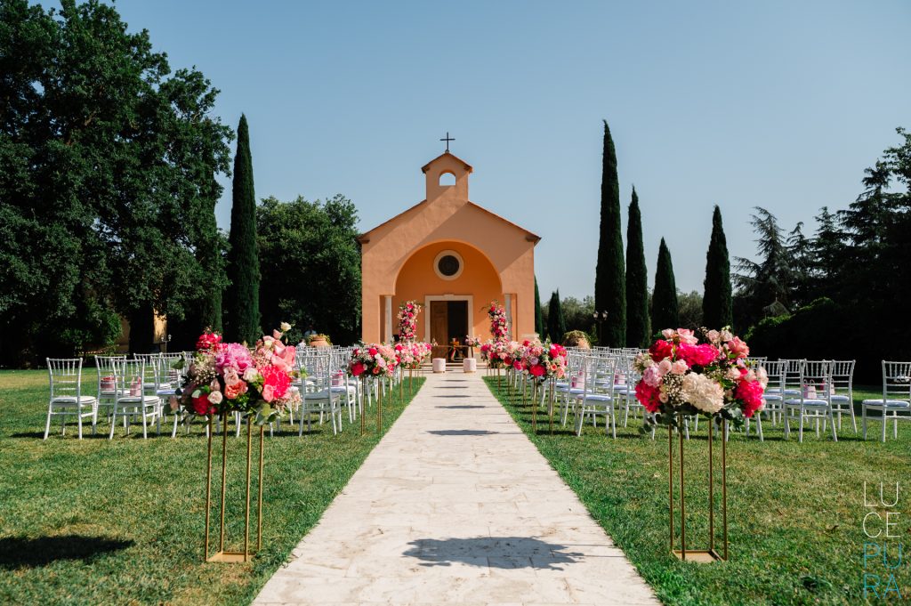 In questa foto si vede una delle caratteristiche dei matrimoni Gen Z, grazie a una cerimonia all’aperto davanti a una piccola cappella, con un corridoio floreale colorato e sedute minimal dal forte impatto visivo.