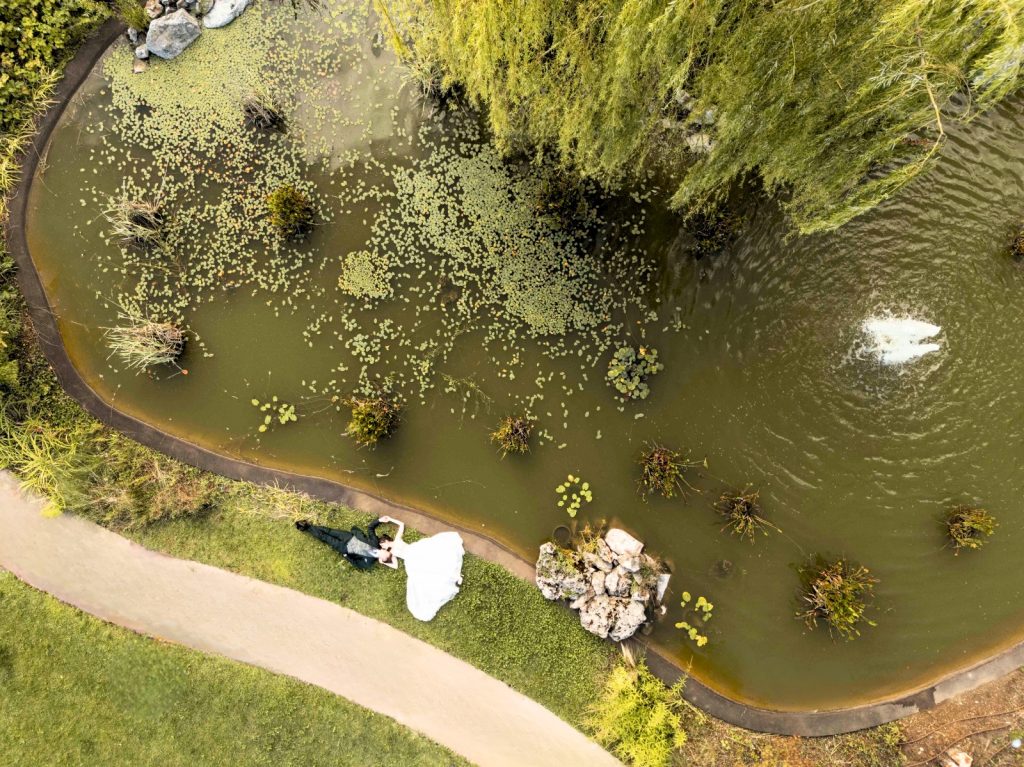 In questa foto si vede uno degli ambienti dedicati al ricevimento matrimonio al Phi Hotel Piajo: uno scatto dall’alto che immortala gli sposi sdraiati sull’erba accanto a un laghetto naturale. Il sentiero sinuoso, la vegetazione acquatica e la fontana creano un’immagine fiabesca e romantica, perfetta per una sessione fotografica da sogno.