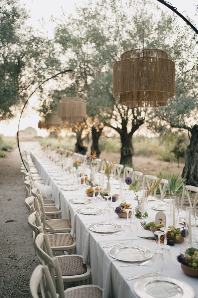 In questa foto di vede una delle caratteristiche dei matrimoni moderni, con una lunga tavolata all’aperto tra ulivi, arredata in modo essenziale e naturale, dove la convivialità diventa parte centrale dell’esperienza.