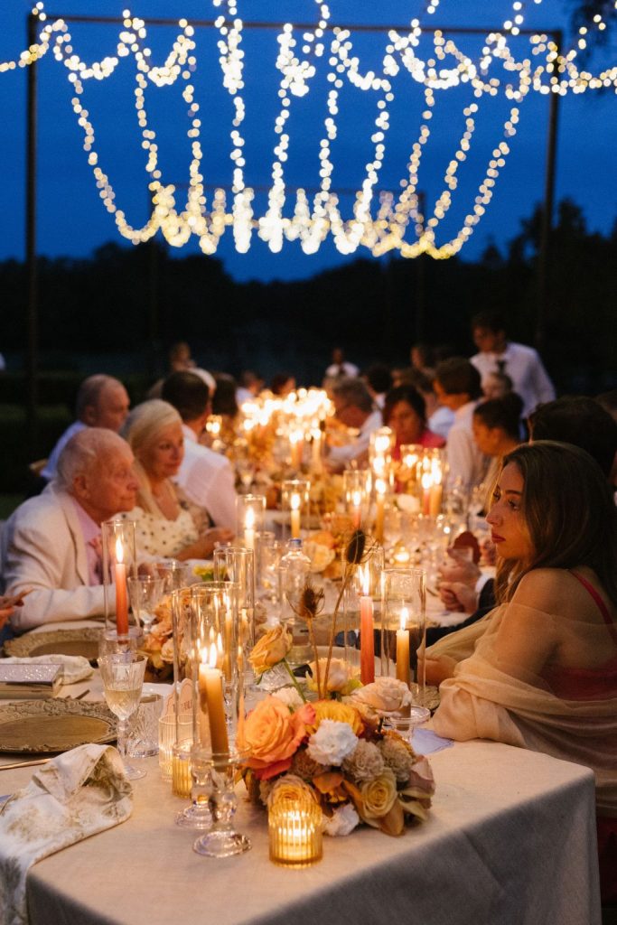 In questa foto si vede uno dei momenti di un matrimonio intimo Villa Francanzan Piovene: una lunga tavolata all’aperto è illuminata dalla luce calda delle candele e da centinaia di micro-luci sospese, che creano un’atmosfera magica e conviviale sotto il cielo blu della sera.