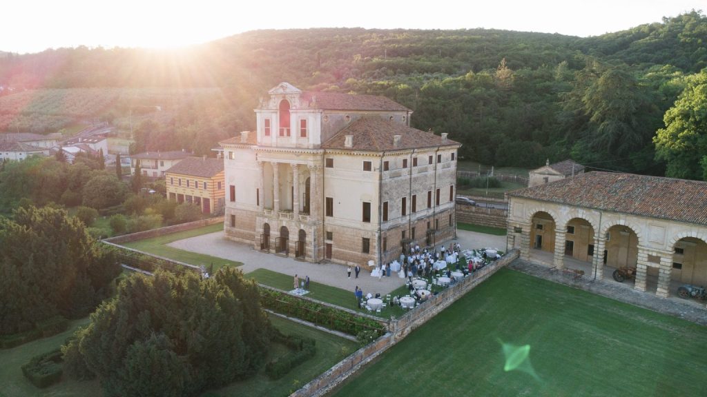 In questa foto si vede uno dei momenti di un matrimonio intimo Villa Francanzan Piovene: un’inquadratura dall’alto mostra la storica villa veneta circondata da colline e alberi, con tavoli apparecchiati nel cortile interno. Il sole al tramonto aggiunge calore alla scena.