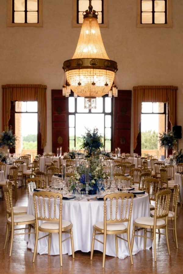 In questa foto si vede uno dei momenti di un matrimonio intimo Villa Francanzan Piovene: la sala interna della villa è allestita con tavoli rotondi, eleganti sedie dorate e centrotavola blu e bianchi. Al centro della stanza troneggia un grande lampadario a gocce, simbolo di raffinatezza.