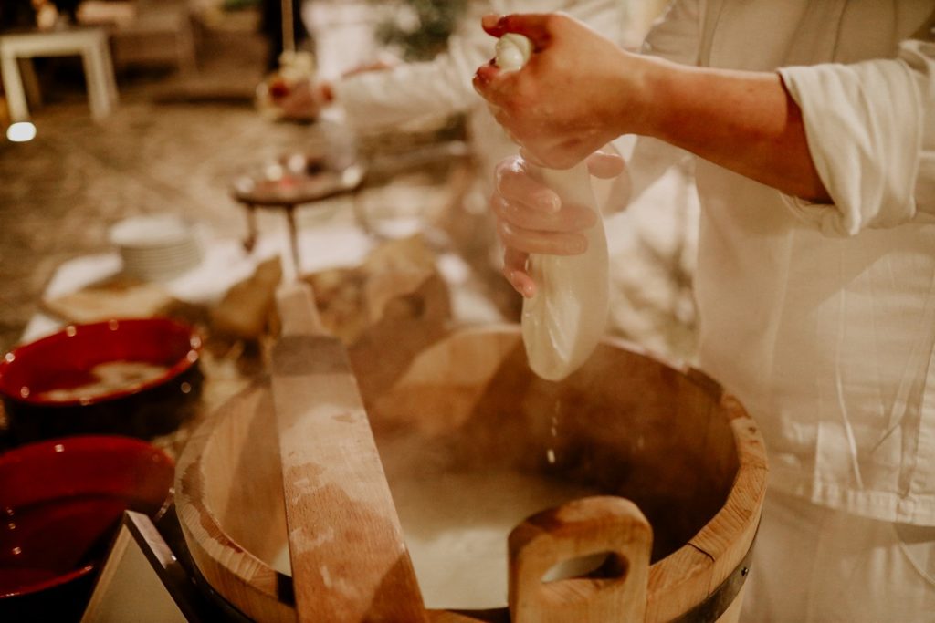 In questa foto si vede uno degli spazi di un matrimonio a a Tenuta Monacelli, un momento di preparazione gastronomica con mani che lavorano una mozzarella fresca sopra una grande madia in legno, simbolo della tradizione culinaria pugliese.