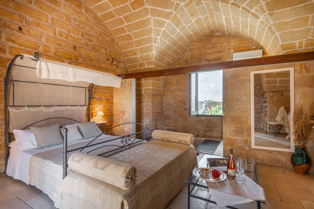 In questa foto si vede uno degli spazi di un matrimonio a a Tenuta Monacelli, una camera in pietra con soffitto a volta, letto matrimoniale con baldacchino e arredi essenziali in stile mediterraneo.