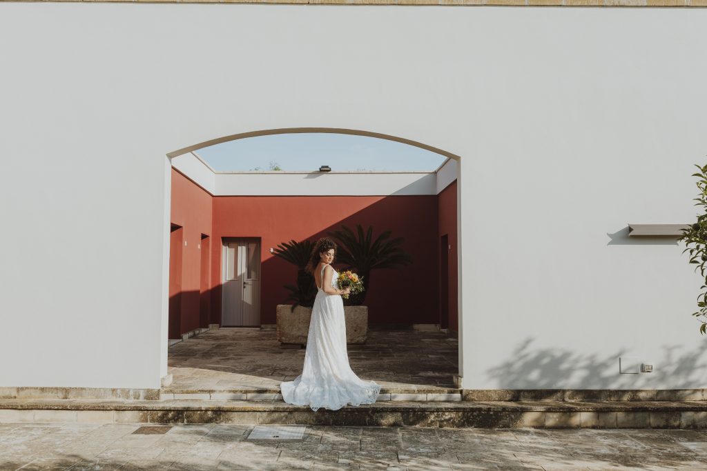 In questa foto si vede uno degli spazi di un matrimonio a a Tenuta Monacelli, la sposa in piedi sotto un arco architettonico minimal, con pareti chiare e un cortile interno dai toni caldi.