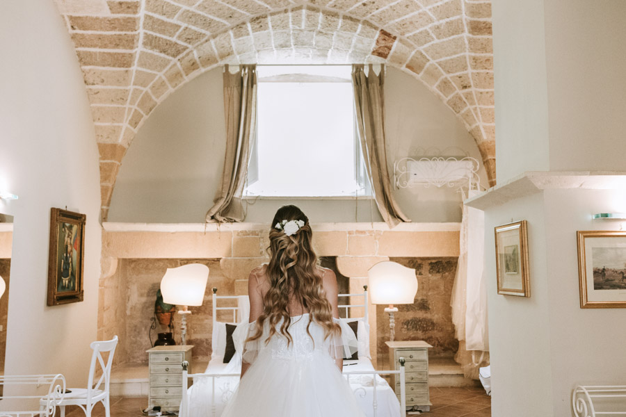 In questa foto si vede uno degli spazi di un matrimonio a a Tenuta Monacelli, una camera nuziale in pietra con soffitto a volta, arredata in stile essenziale, con la sposa di spalle al centro della stanza.