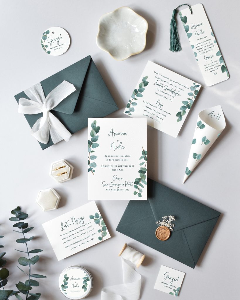 In questa foto si vede una delle tendenze partecipazioni matrimonio 2026: un coordinato ispirato alla natura, con illustrazioni di foglie di eucalipto su cartoncini bianchi. Le buste sono verde salvia e alcuni elementi sono chiusi con un sigillo in ceralacca o un nastro bianco leggero. Oltre alla partecipazione, ci sono etichette, coni per il riso, tag personalizzati e cartoncini di ringraziamento: un set coordinato che comunica armonia, freschezza e attenzione ai dettagli.