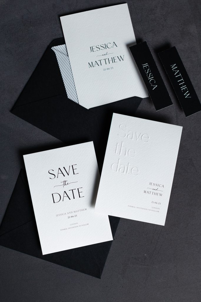 In questa foto si vede una delle tendenze partecipazioni matrimonio 2026: un coordinato grafico elegante e monocromatico con buste nere e cartoncini bianchi. I caratteri sono neri e moderni, con una variante impressa in rilievo. Le scritte “Save the Date” e i nomi Jessica e Matthew spiccano su fondo chiaro. Il design gioca con contrasti grafici e texture tattili, dando vita a un invito dal tono urbano, sofisticato e senza tempo.