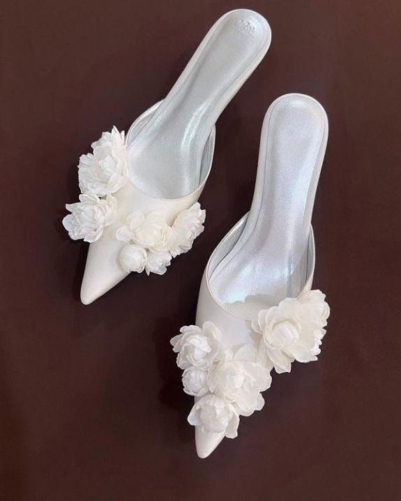 In questa foto si vede una proposta di scarpe da sposa 2026, mules bianche a punta con applicazioni floreali tridimensionali sul davanti, pensate come alternativa romantica e moderna al sandalo classico.