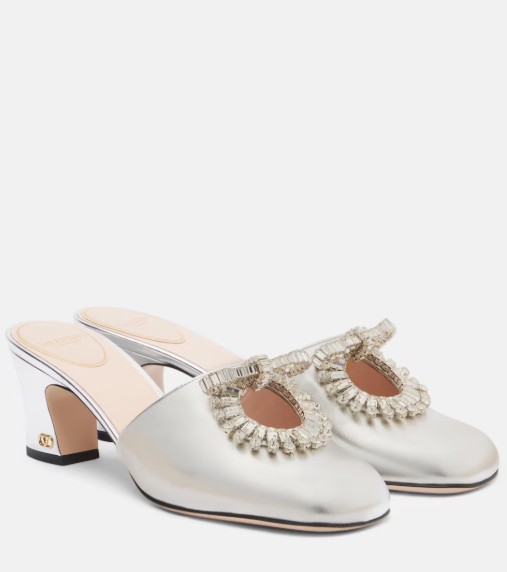 In questa foto si vede una proposta di scarpe da sposa 2026, mules bianche con tacco medio e applicazioni gioiello sul davanti, dal design elegante ma rilassato.