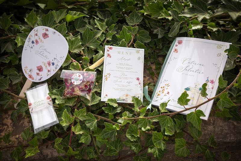 In questa foto, una stationery composta da ventaglio, fazzolettini, petali per il lancio, menù e libretto cerimonia nei toni del rosa e del lilla