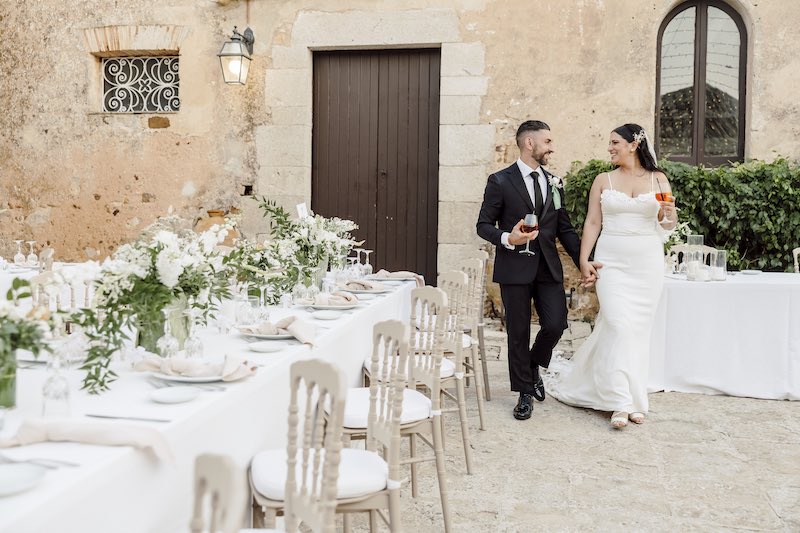 In questa foto, due sposi sorridenti mentre camminano tra i tavoli del loro matrimonio allestito dall'Atelier Cianfoni con colori neutri