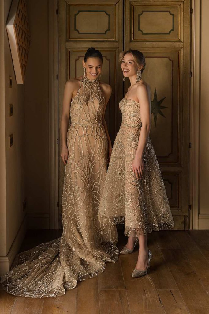 In questa foto, due modelle ridono indossando due abiti della collezione sposa Donatella Gallo 2027: a destra un modello lungo con scollo all'americana; a sinistra un modello corto ad A