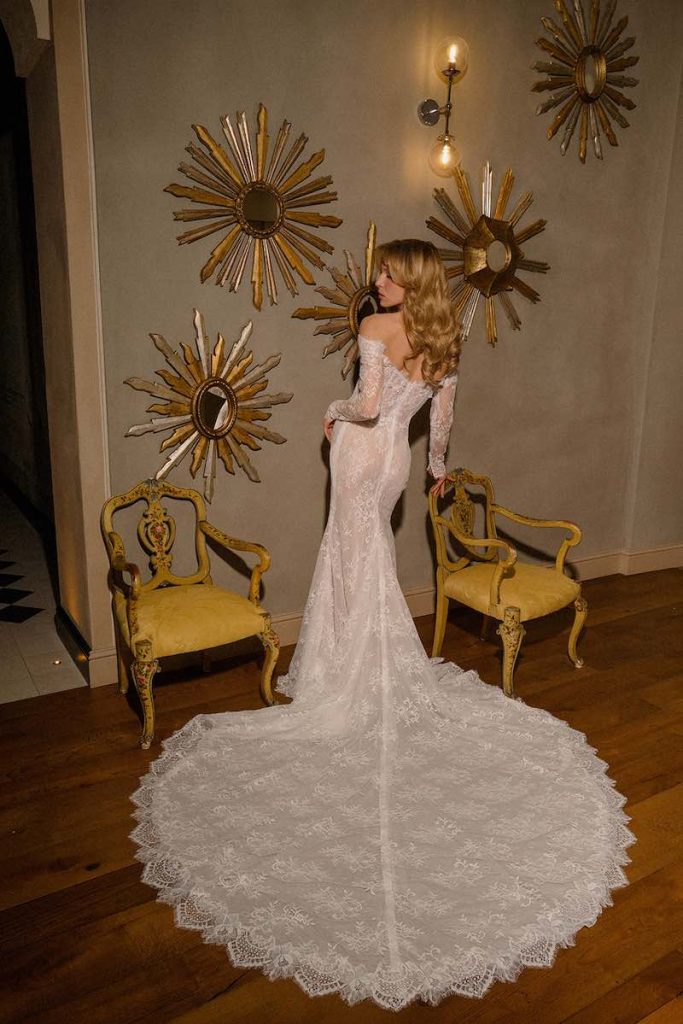 In questa foto, una modella posa di spalle indossando un abito da sposa in pizzo ricamato con manicotti abbinati