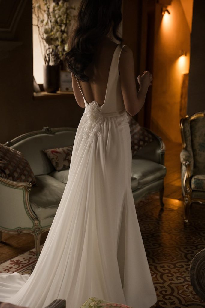 In questa foto una modella di spalle posa indossando un abito da sposa Donatella Gallo 2027, modello scivolato in seta con ricamo 3D floreale sulla schiena