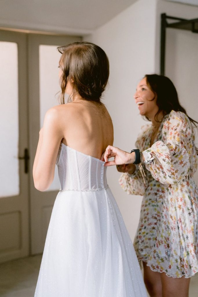 In questa foto, Nunzia Apicella founder di Le Papillon Event Designer mentre aiuta una sposa ad indossare il suo abito e ride