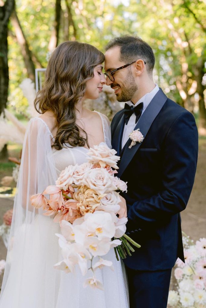 In questa foto, due sposi che si guardano innamorati. In primo piano un bouquet di rose e orchidee nei torni del rosa chiaro