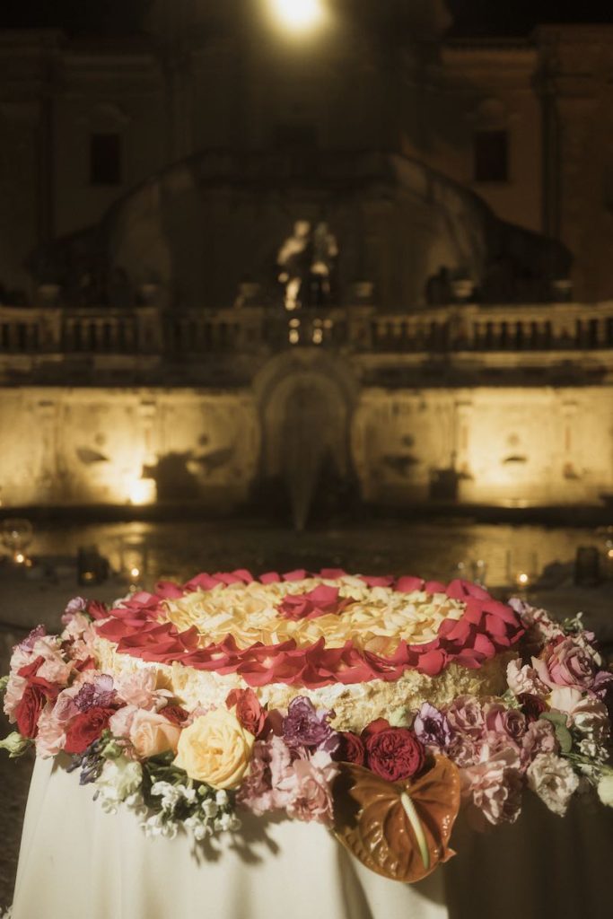 In questa foto, una torta nuziale ad un piano decorata con petali e fiori multicolor