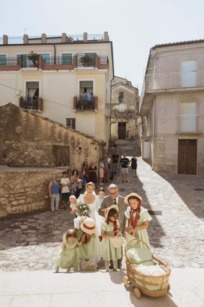In questa foto, una sposa entra in chiesa al braccio del padre e preceduta dalle sue Flower Girl