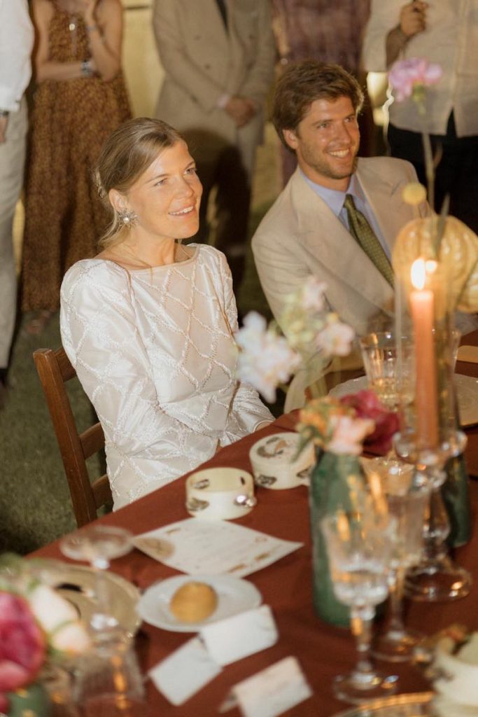 In questa foto, due sposi sorridenti mentre ascoltano i discorsi dei loro amici durante il ricevimento