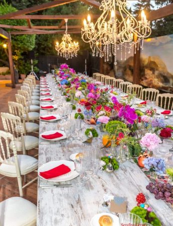 In questa foto una mise en place in stile Boho Chic nei colori fuxia, arancione, azzurro e rosso realizzato sulla terrazza esterna di Villa Boscogrande a Palermo