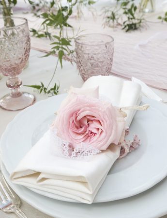 In questa foto una mise en place elegante nei colori del rosa e del bianco. Il fermatovagliolo è realizzato con una rosa in coordinato