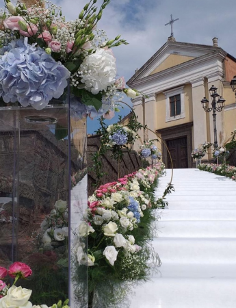 In questa foto l'allestimento della scalinata di una chiesa per un matrimonio religioso. La scalinata e rivestita da un tappeto bianco mentre sui bordi sono disposti fiori bianchi e fuxia e ortensie azzurre