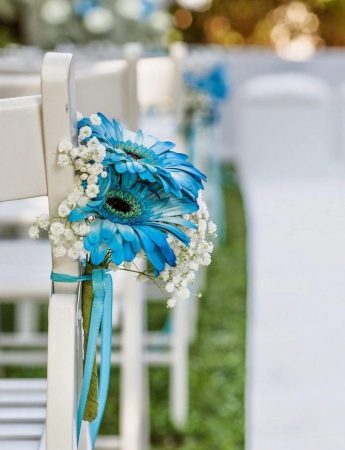 In questa foto il dettaglio di un allestimento per un rito civile nei colori bianco e azzurro. Alle sedie sono legati piccoli bouquet di girasoli azzurri e velo da sposa