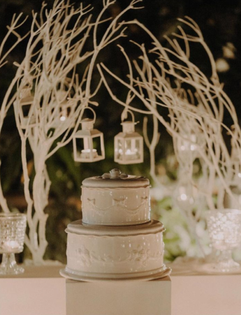 In questa foto di sera il tavolo di una confettata per matrimonio con portaconfetti in porcellana e cristallo e piccole lanterne bianche con candele accese appese a rami bianchi