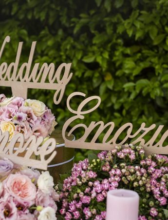 In questa foto tre scritte colore oro poggiate su fiori rosa e bianchi riportano le parole "Wedding", "Emozione", "Amore"