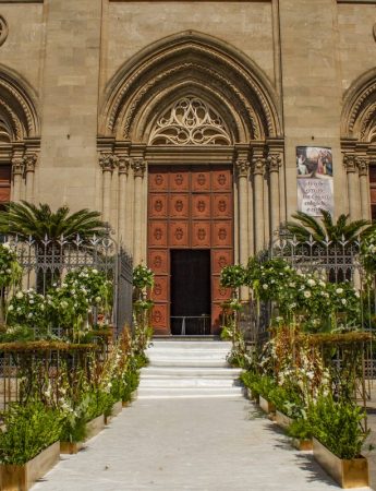 In questa foto l'ingresso di una chiesa decorata con fiori e alberi disposti sulla scalinata coperta da un tappeto bianco