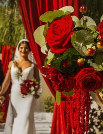 In questa foto due sposi fanno il loro ingresso nella location delle nozze attraverso un sipario rosso. Le decorazioni e il bouquet sono di rose rosse